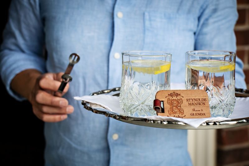 Paul Manshon greeting guests at The Reynolds Mansion with a silver tray of lemon water and the Glenda room key — the personal welcome that begins every stay at this historic Asheville bed and breakfast