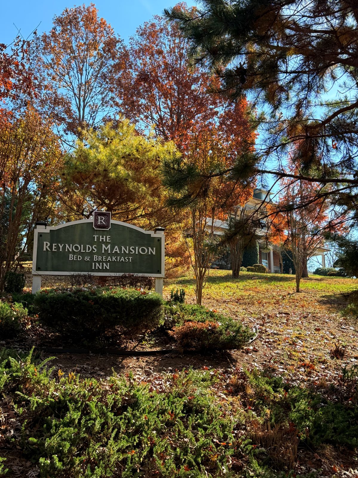 The Reynolds Mansion Bed and Breakfast Inn sign surrounded by brilliant autumn foliage, the historic brick mansion visible through the trees on Reynolds Mountain in Asheville, North Carolina