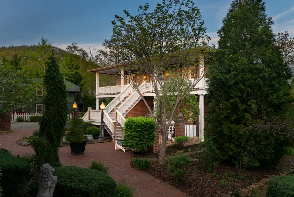 The Carriage House at dusk, its lamplit staircase and brick garden path winding through clipped greenery.