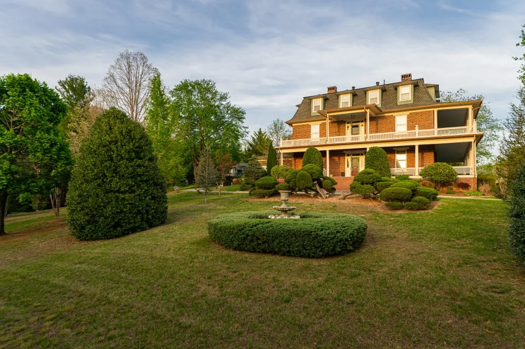 The mansion seen across its open front lawn and clipped boxwood garden on a clear spring day.