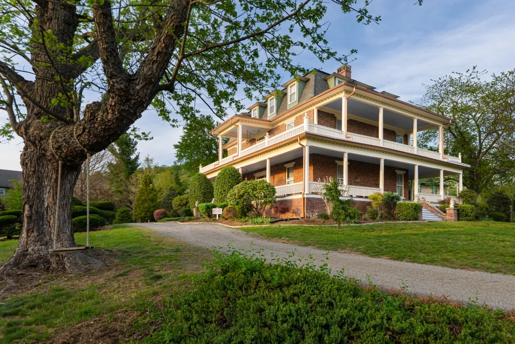 A wooden swing hanging from a large shade tree beside the gravel drive, with the three-story mansion and its wrap-around porches behind.