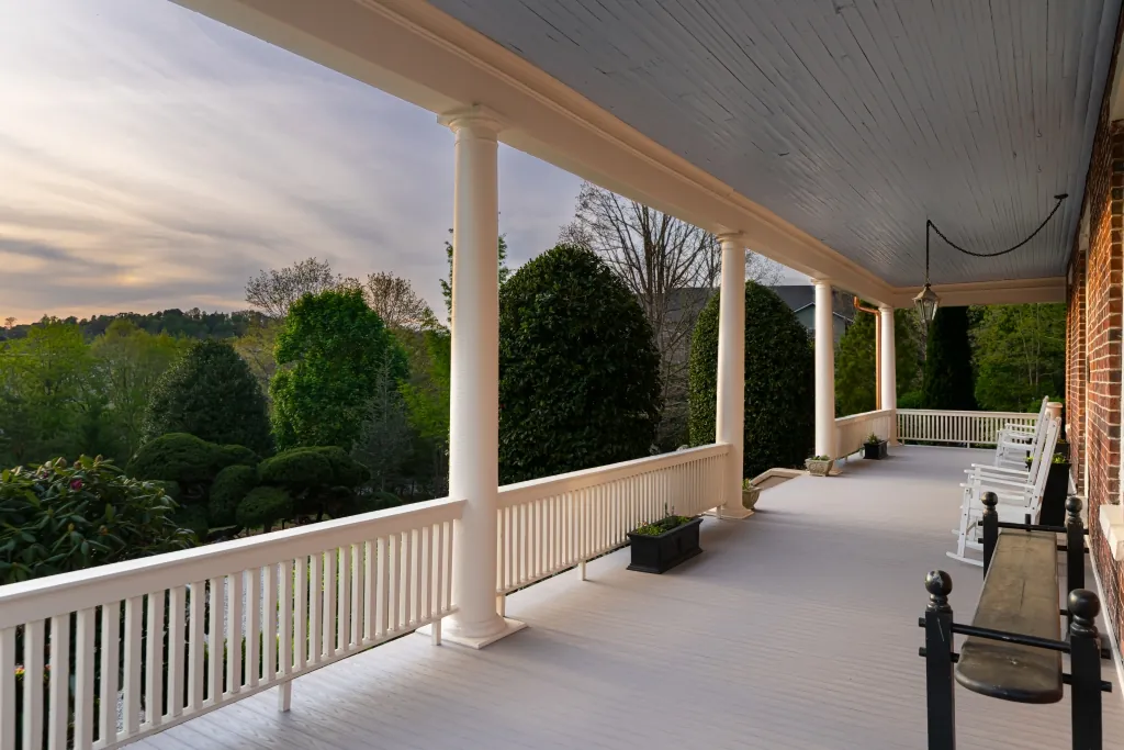The wrap-around porch at sunset, lined with white rocking chairs, looking out over the gardens toward the hills.