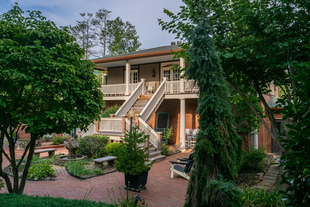 The Carriage House and its exterior staircase seen through summer trees, with brick paths and garden beds below.