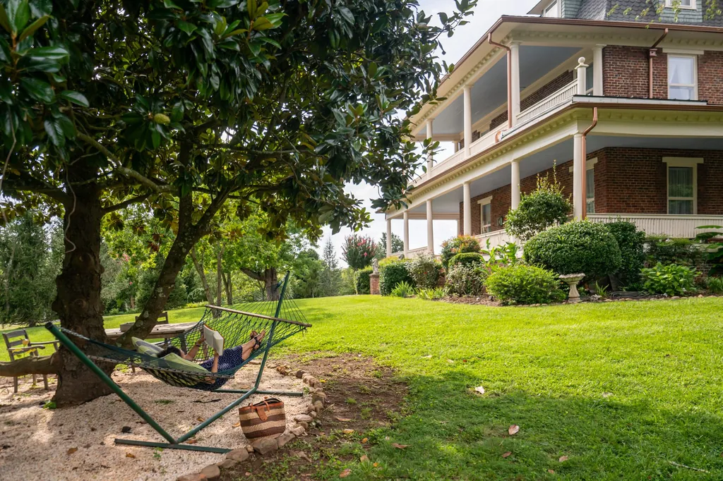 A rope hammock strung beneath the old magnolia, with the mansion’s porches showing through the leaves behind.