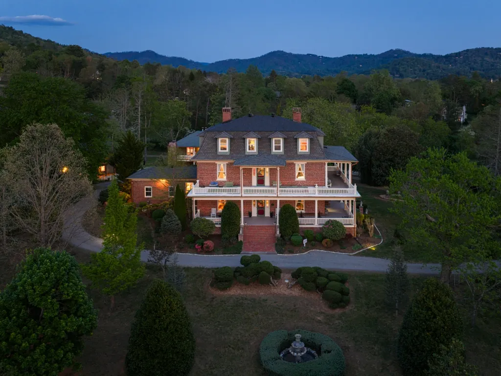 An evening view of the mansion with warm light in its windows and the mountains in silhouette beyond.