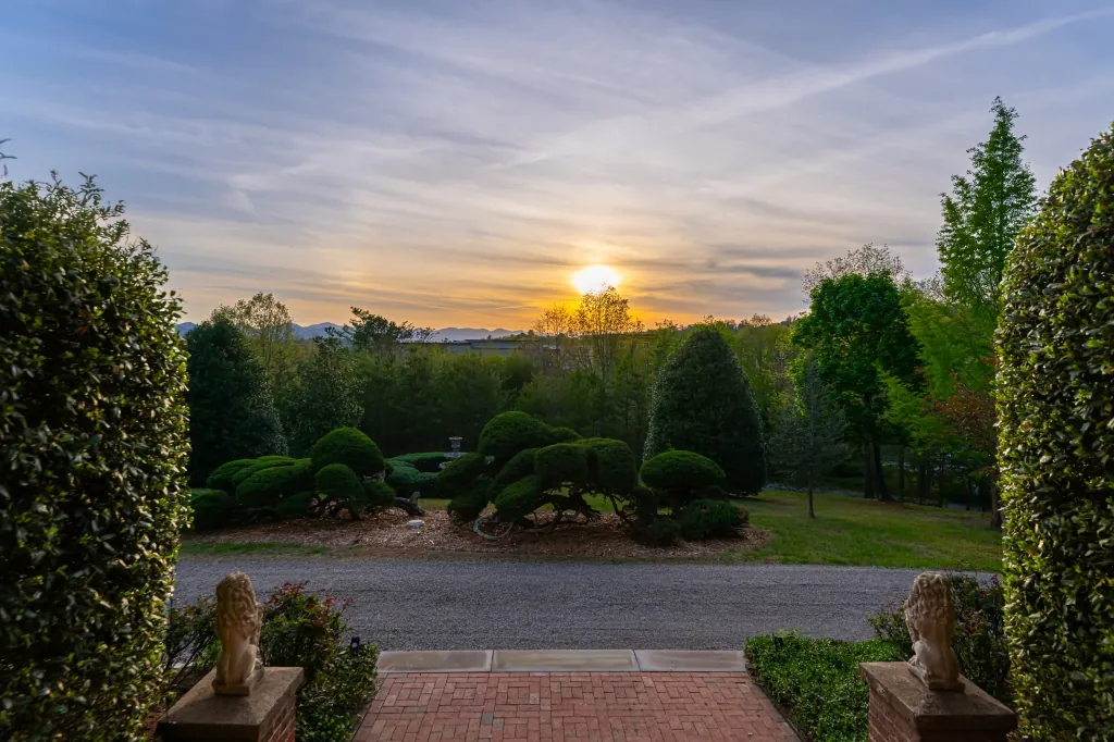 The sun setting over the topiary garden and distant mountains, viewed between two stone lions at the front walk.