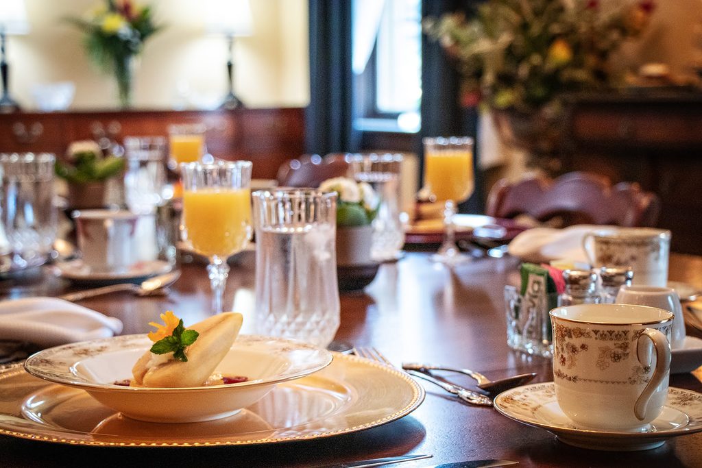 An elegant breakfast table set with crystal, fine china, mimosas, and a plated course in the dining room at The Reynolds Mansion