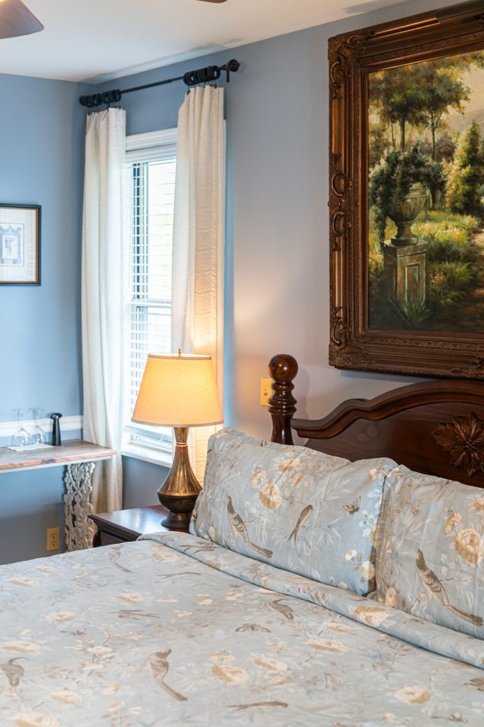 Blue Hydrangea suite — bedside detail with antique lamp and gold-framed painting at The Reynolds Mansion