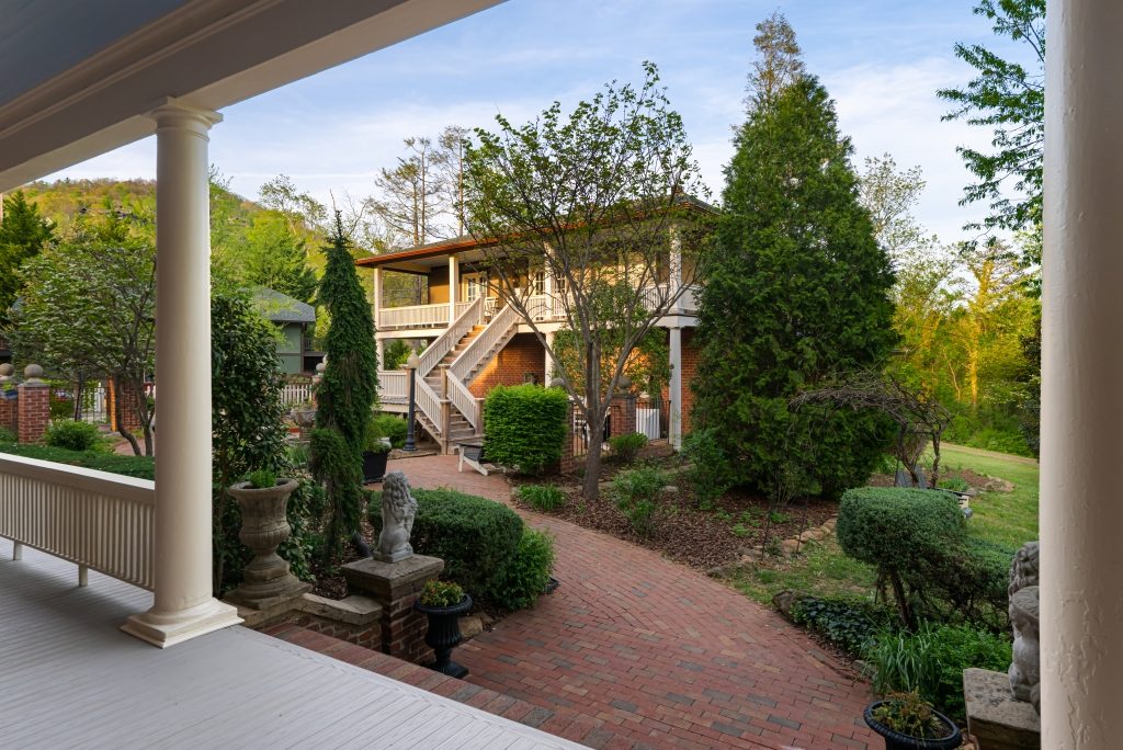 The Carriage House at The Reynolds Mansion seen from the main mansion's porch — just steps across the brick courtyard with garden landscaping and a peek of the mountains beyond