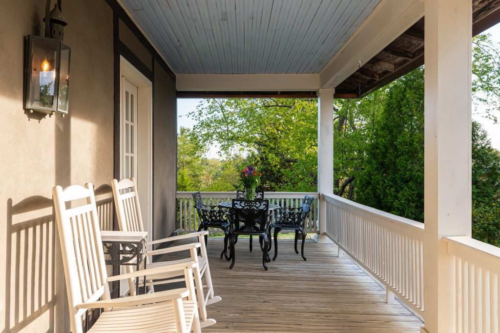 Carriage House covered porch with white rocking chairs and bistro seating overlooking the property