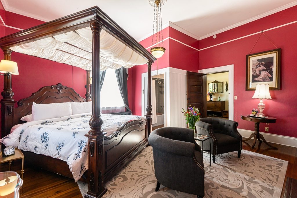Claudette room — king canopy bed with crimson walls, gas fireplace, two armchairs and period painting at The Reynolds Mansion