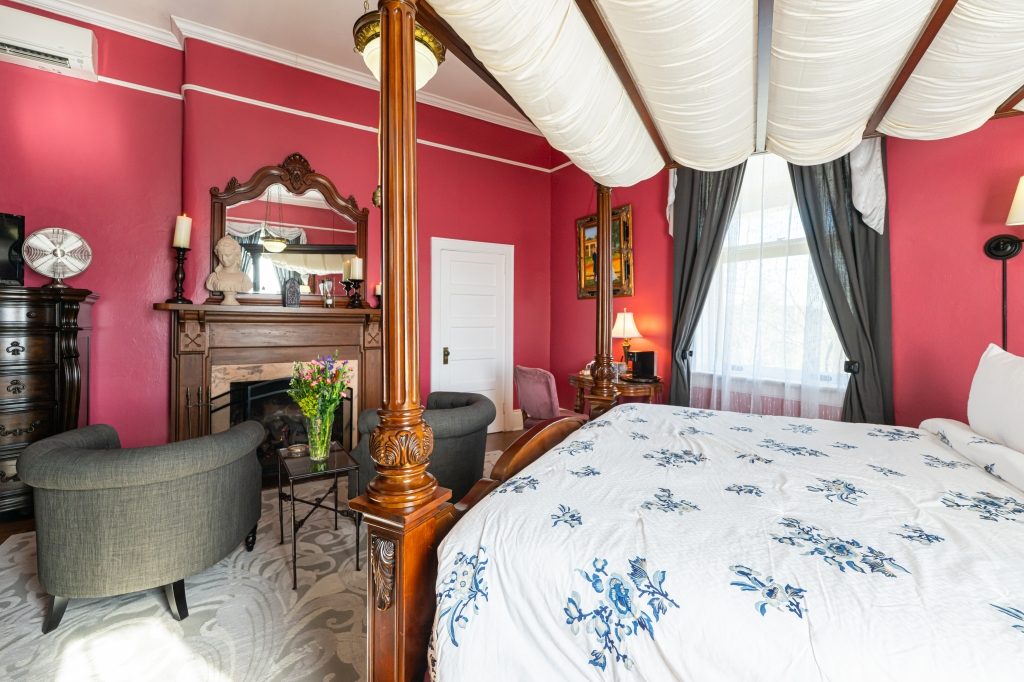 Claudette room — king canopy bed with carved post and gas fireplace at The Reynolds Mansion