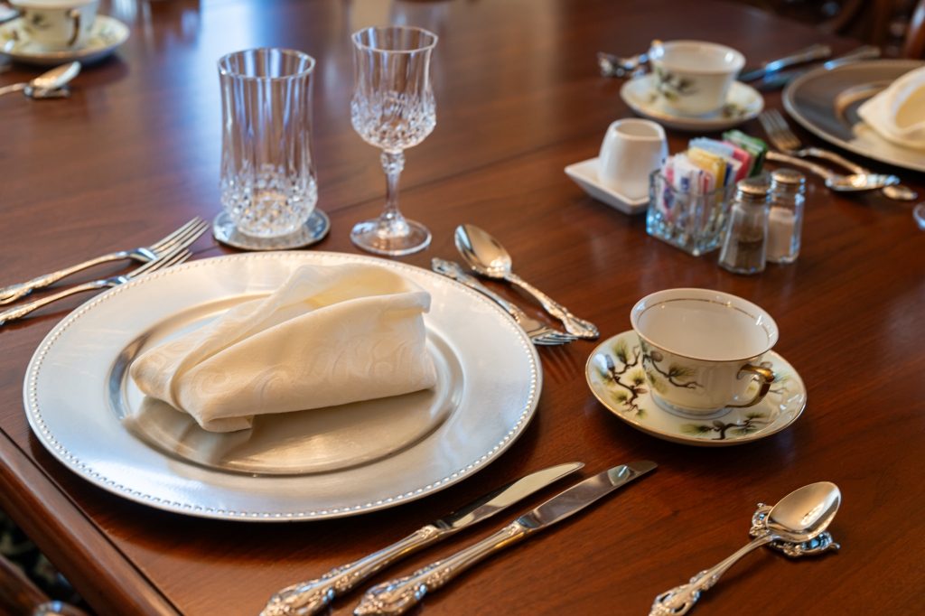 Place setting detail — silver charger, hand-painted china teacup, and crystal stemware on the mahogany table at The Reynolds Mansion