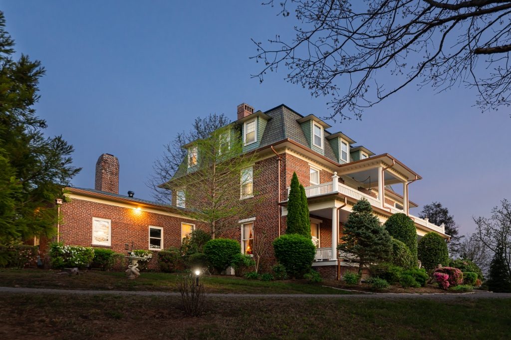 Side view of The Reynolds Mansion at dusk showing original 1847 brick, mansard roof with dormers, and double porches