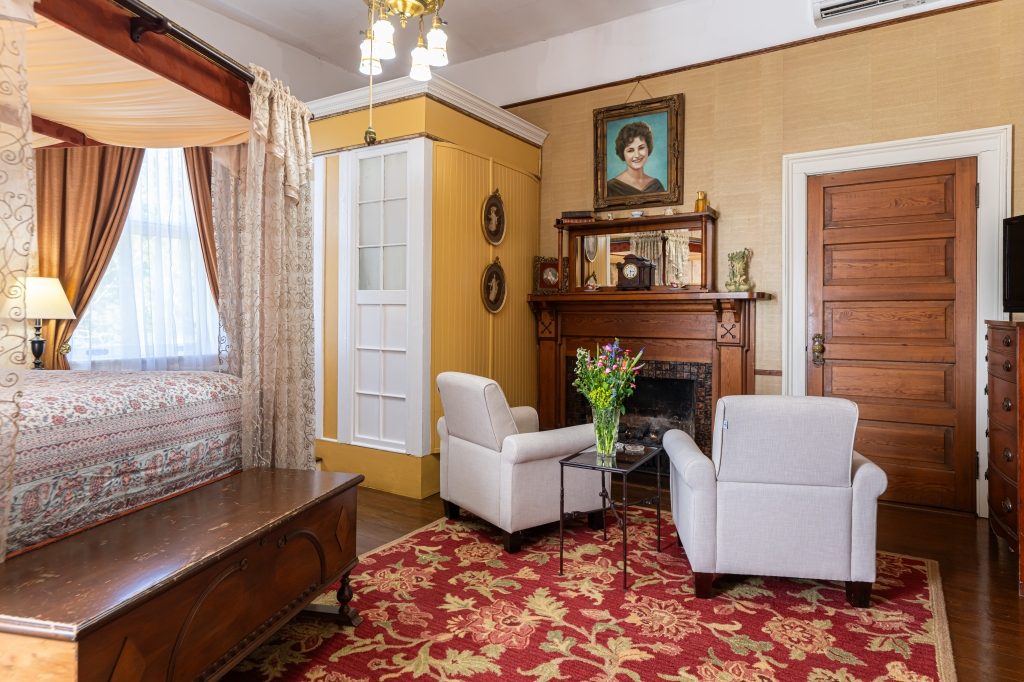 Glenda room sitting area — white armchairs, cedar chest, gas fireplace and period portrait at The Reynolds Mansion