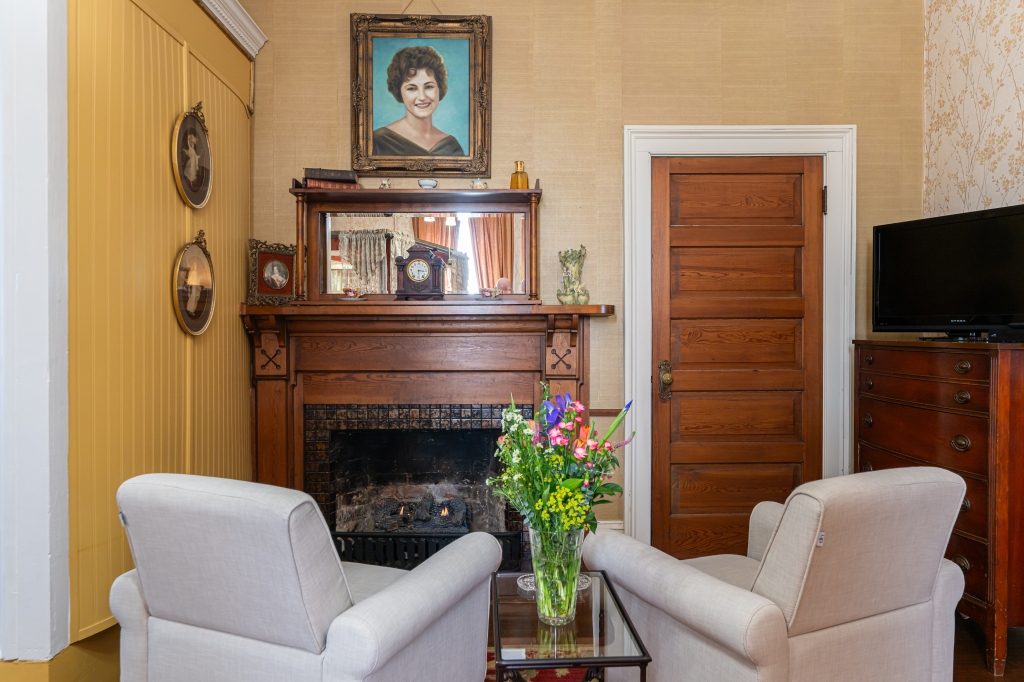 Glenda room fireplace — gas fireplace with carved mantel, period portrait, and oval portraits on the wall at The Reynolds Mansion