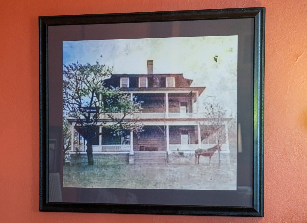 Historic photograph of The Reynolds Mansion — the original brick structure with wraparound porches and a horse in the foreground, late 1800s to early 1900s, framed and displayed at the mansion
