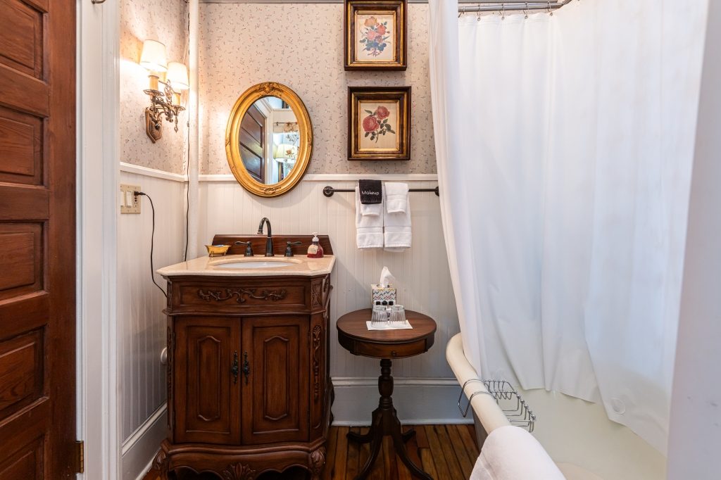 Katie room private bathroom — claw foot tub, ornate gold mirror over wood vanity, and framed prints at The Reynolds Mansion