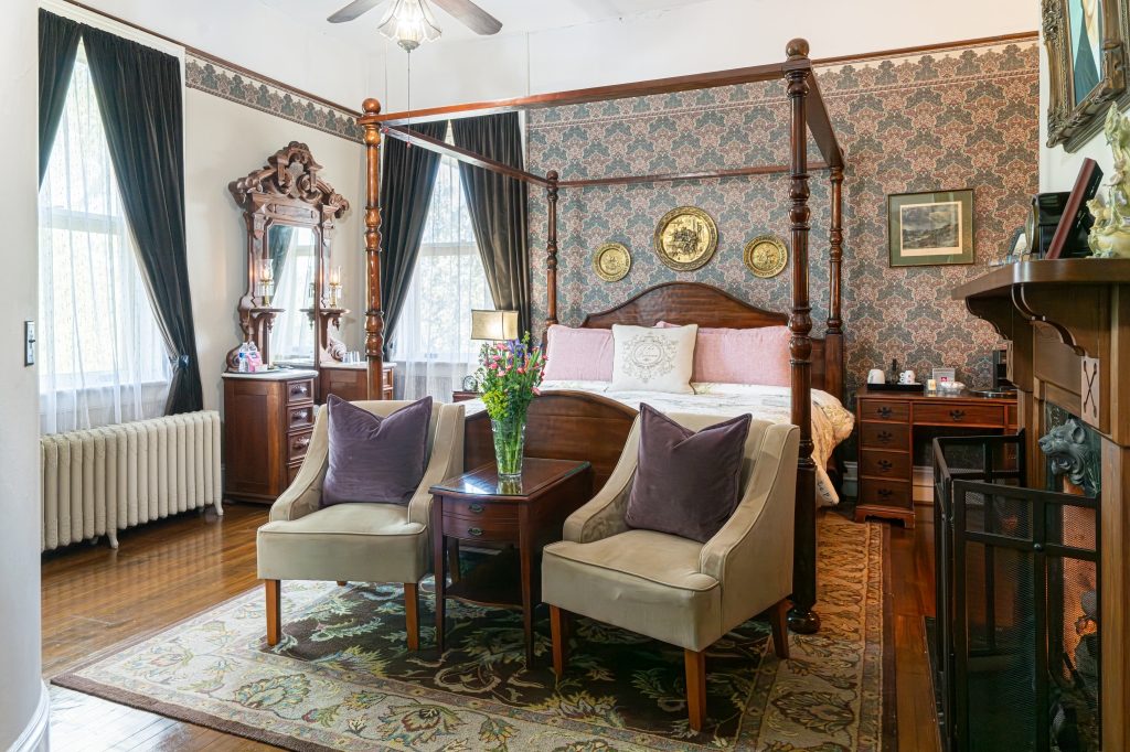Linda room — king four-poster canopy bed with paisley wallpaper, sitting area, and gas fireplace at The Reynolds Mansion