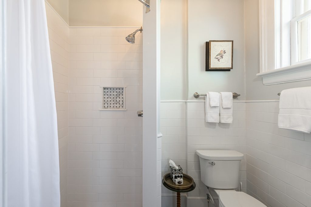 Linda room private bathroom — white subway tile shower stall, bird artwork at The Reynolds Mansion
