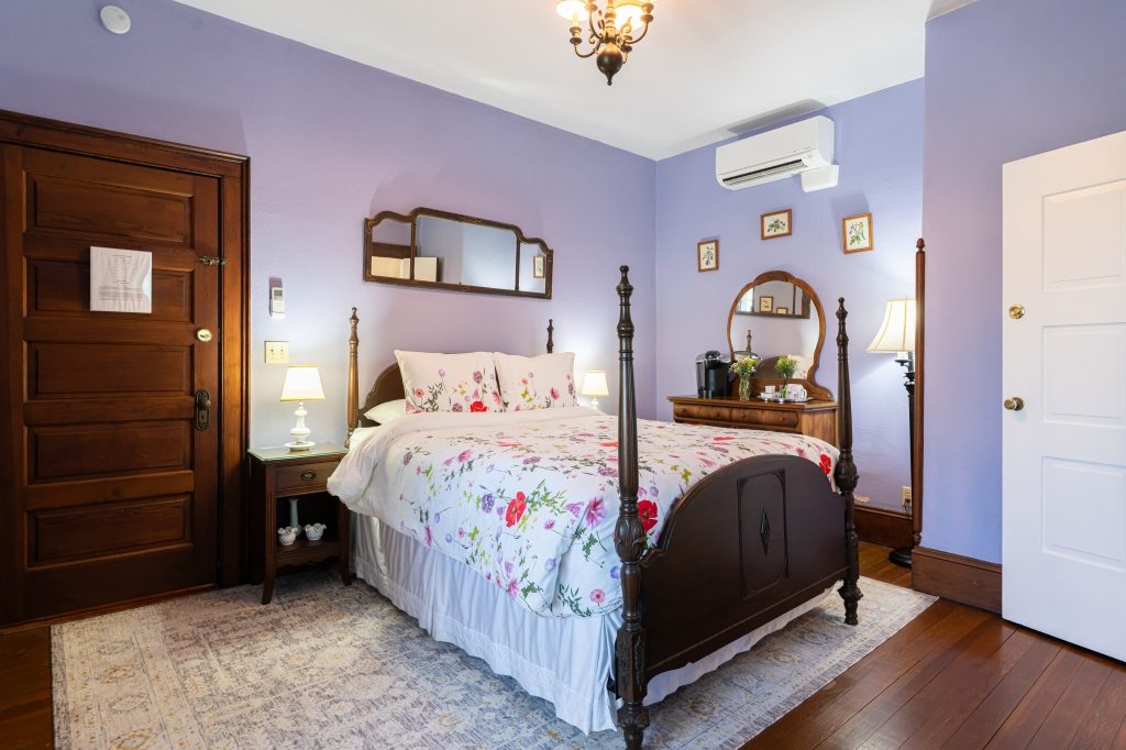 Maggie room — four-poster wood bed with floral linens against lavender walls at The Reynolds Mansion