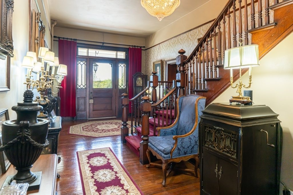 Grand foyer at The Reynolds Mansion with antique staircase, leaded glass front door, and period furnishings from the original 1847 home