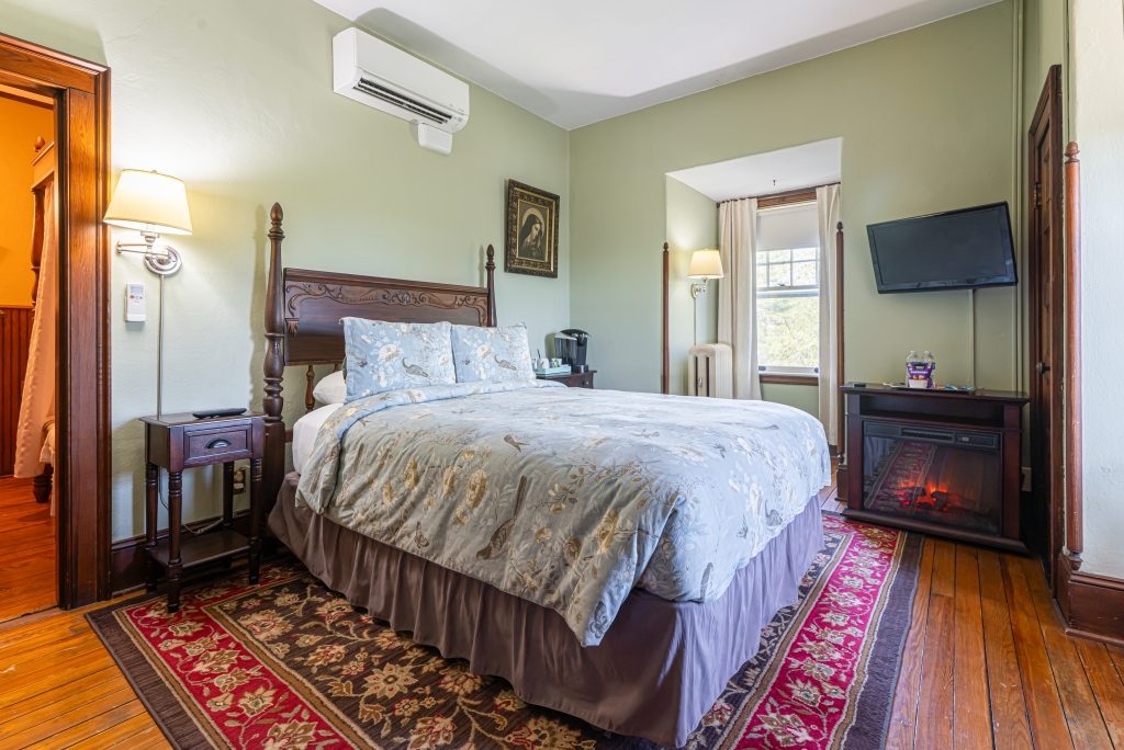 Vera room — third-floor queen four-poster bed with sage walls, electric fireplace, and period painting at The Reynolds Mansion