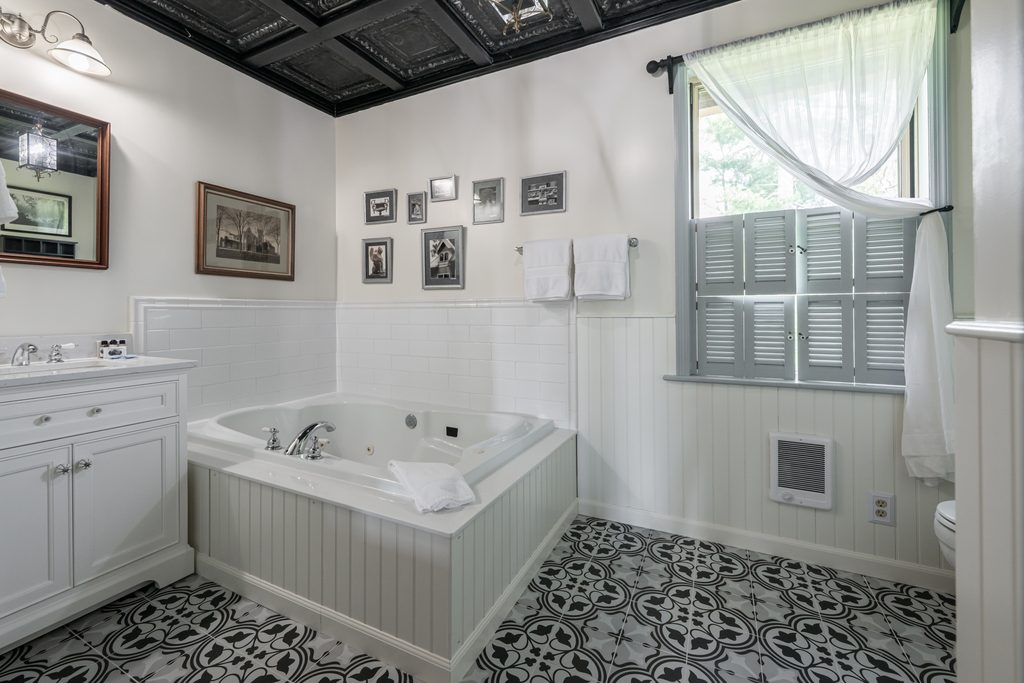 All That Jazz suite — private bathroom with Jacuzzi tub, pressed-tin ceiling, and black-and-white patterned tile floor at The Reynolds Mansion Carriage House