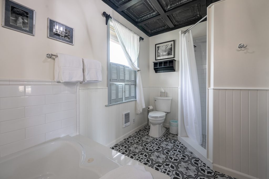 All That Jazz suite — private bathroom with walk-in shower, Jacuzzi tub, and shuttered window under the pressed-tin ceiling at The Reynolds Mansion Carriage House