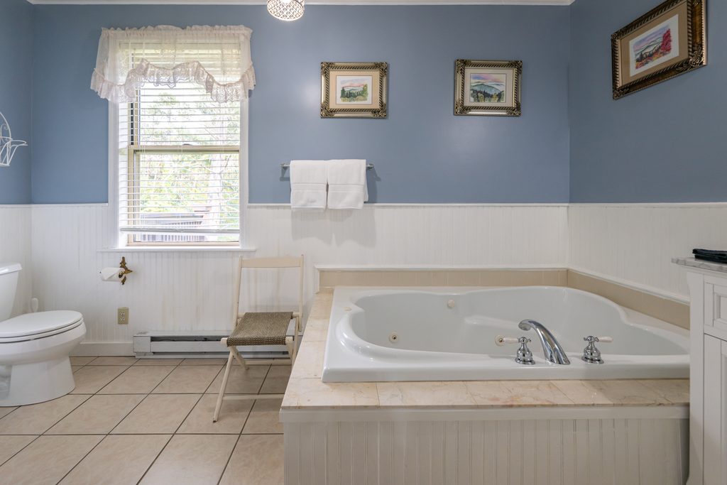 Blue Hydrangea suite — private bathroom with Jacuzzi tub, periwinkle-blue walls, and white wainscoting at The Reynolds Mansion Carriage House