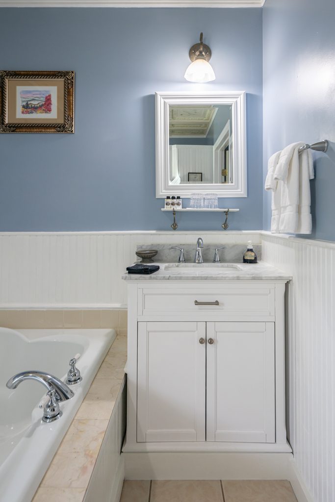 Blue Hydrangea suite — white vanity with mirrored cabinet and sconce beside the tub at The Reynolds Mansion