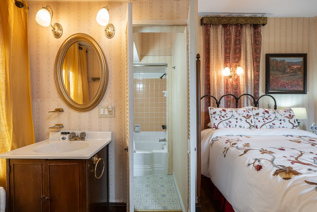 Inez room — en-suite bath entry with oval mirror, marble-top vanity, and sconce lighting at The Reynolds Mansion