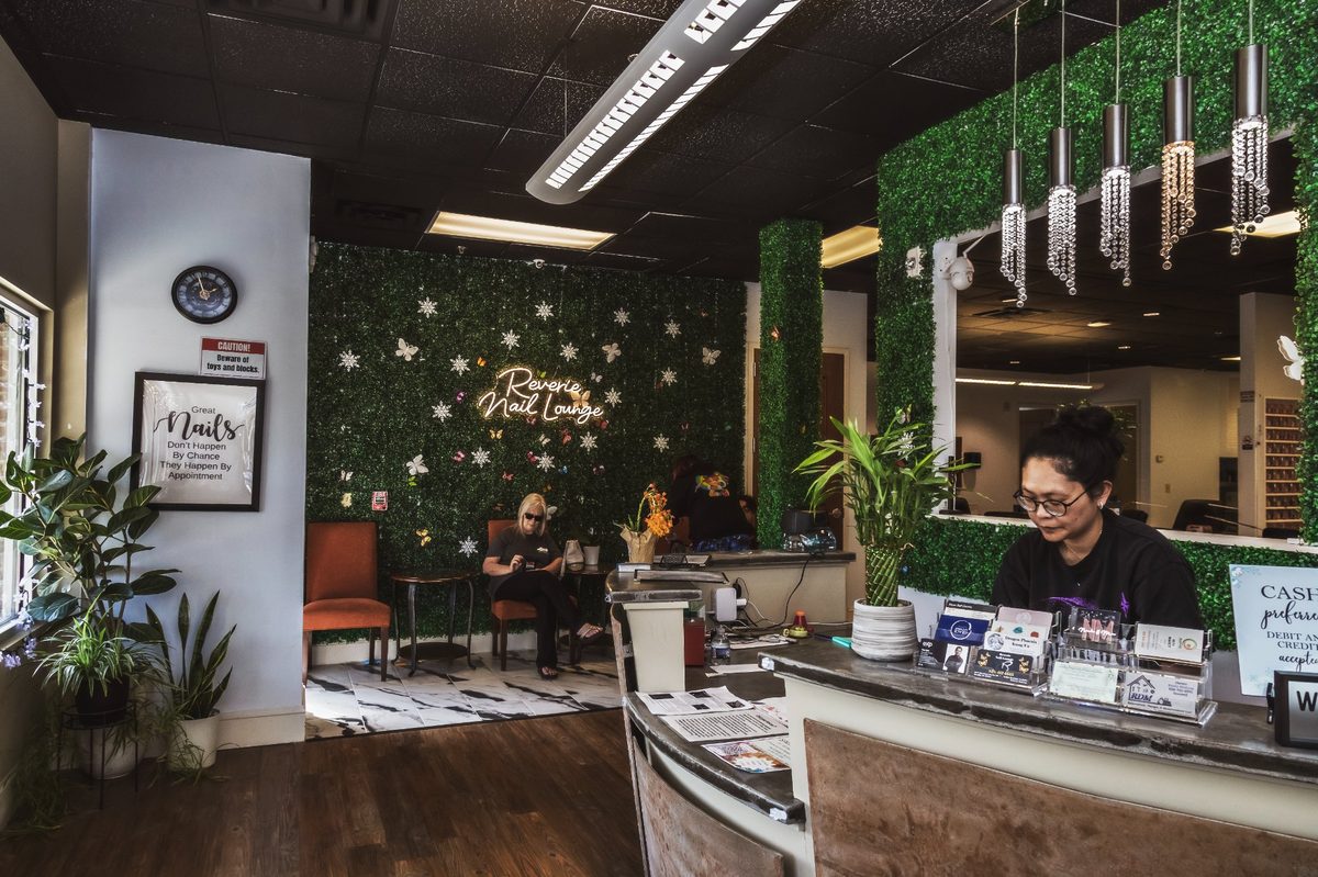Reverie Nail Lounge interior — neon sign, green plant wall, and reception desk
