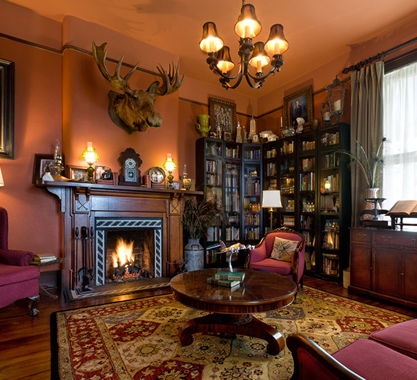 Cozy vintage room with a lit fireplace, bookshelves, and a moose head on the wall.