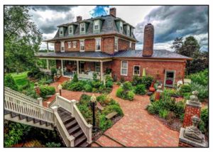 A Victorian-style house with a wrap-around porch and a landscaped brick courtyard.