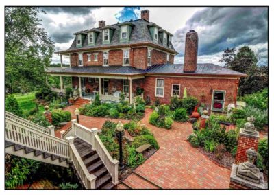 A Victorian-style house with a wrap-around porch and a landscaped brick courtyard.
