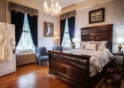 Elegant bedroom with a large bed, chandelier, and dark curtains against a window.