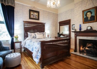 Elegant bedroom with a wooden bed, fireplace, chandelier, and patterned wallpaper.