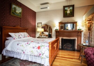 Cozy vintage bedroom with floral bedding, a wooden fireplace, and hardwood floors.