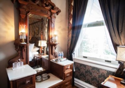 Elegant vintage bathroom with ornate wooden vanity and mirror, adjacent window with dark drapes.