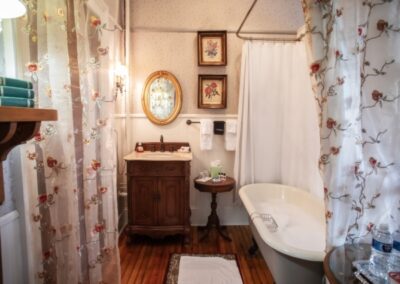 Vintage bathroom with claw-foot tub, pedestal sink, wooden floors, and floral wallpaper.