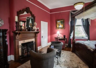 Elegant living room with deep red walls, a fireplace, ornate mirror, and stylish seating.