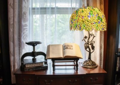 A cozy reading nook with an open book on a stand, a colorful lamp, and a window with sheer curtains.