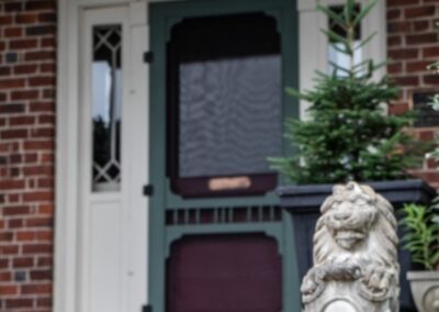 Front door of a brick house with a lion statue and red flowers.