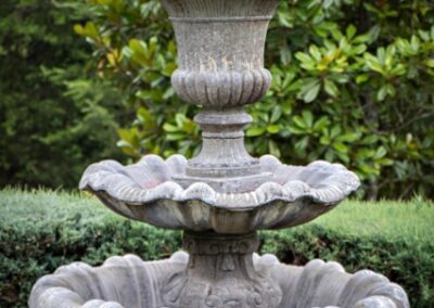 An ornate three-tiered stone fountain amidst lush greenery.