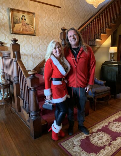 Two people posing in a cozy room, one in a Santa-inspired outfit and the other in a red jacket.