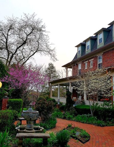 Quaint brick house with a blossoming garden and pathway under an overcast sky.