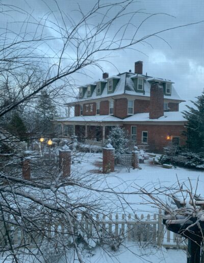 A large brick house surrounded by snow-covered trees during twilight.